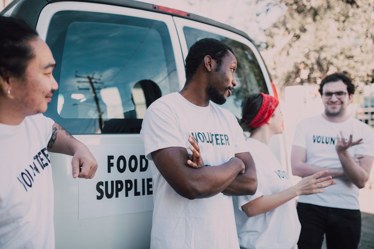Volunteers gather beside a van to prepare and distribute food supplies outdoors.