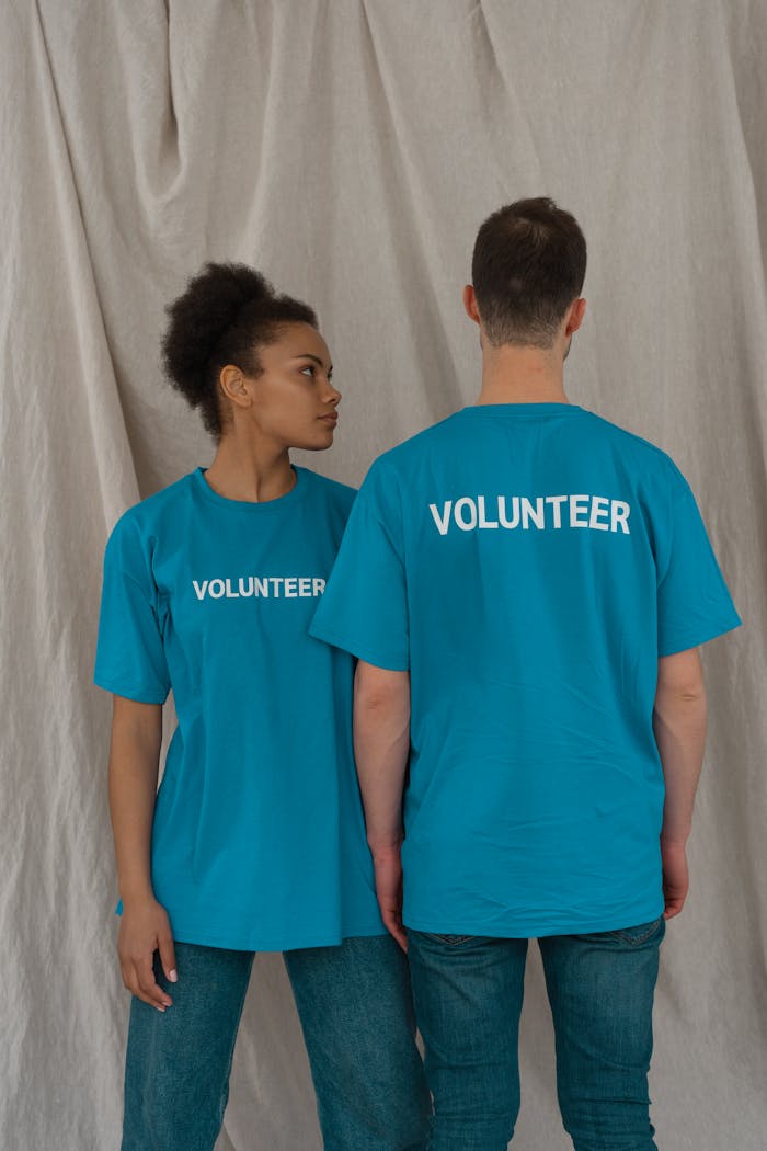 Two diverse volunteers standing in blue shirts with volunteer text, studio setting.